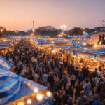Pasillos llenos y stands iluminados en la Feria del Libro de Kolkata al atardecer; pabellón del país tema con colores celeste y blanco.