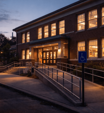 Fachada de una biblioteca pública con acceso por rampa, al atardecer.