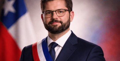 Retrato editorial de Gabriel Boric con traje, corbata y banda presidencial, con bandera de Chile desenfocada al fondo.