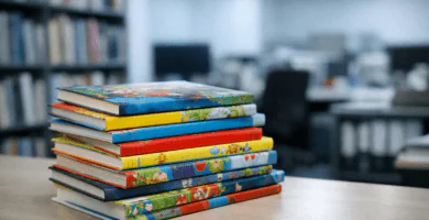 Pila de libros infantiles sobre una mesa en una oficina editorial, con estanterías desenfocadas al fondo.