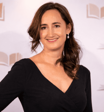 Retrato editorial de una escritora en un photocall de premios literarios, con vestido negro y fondo neutro sin texto.