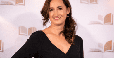 Retrato editorial de una escritora en un photocall de premios literarios, con vestido negro y fondo neutro sin texto.
