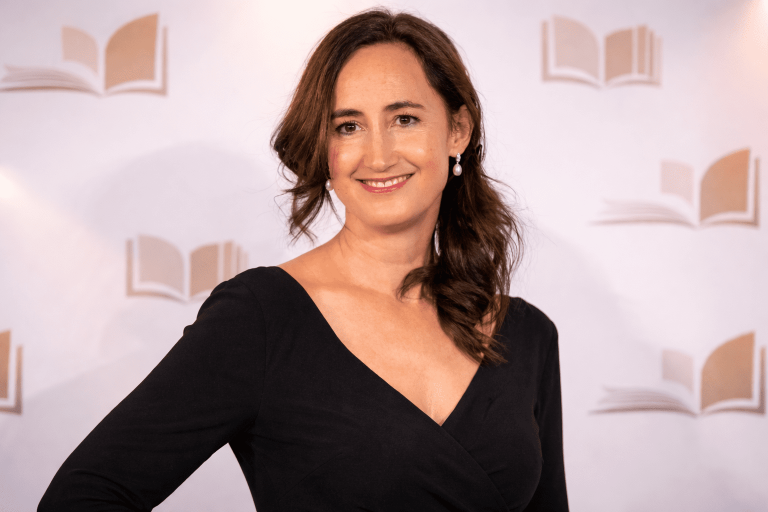 Retrato editorial de una escritora en un photocall de premios literarios, con vestido negro y fondo neutro sin texto.