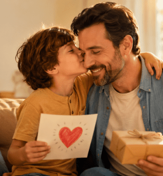 Padre recibiendo un beso de su hijo con tarjeta y regalo del Día del Padre en un ambiente cálido y familiar.