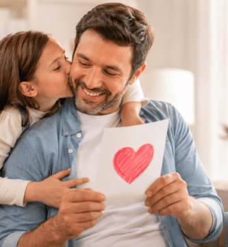 Papá sonríe mientras recibe una tarjeta del Día del Padre con un corazón dibujado y un beso de su hija