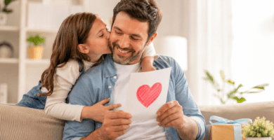 Papá sonríe mientras recibe una tarjeta del Día del Padre con un corazón dibujado y un beso de su hija