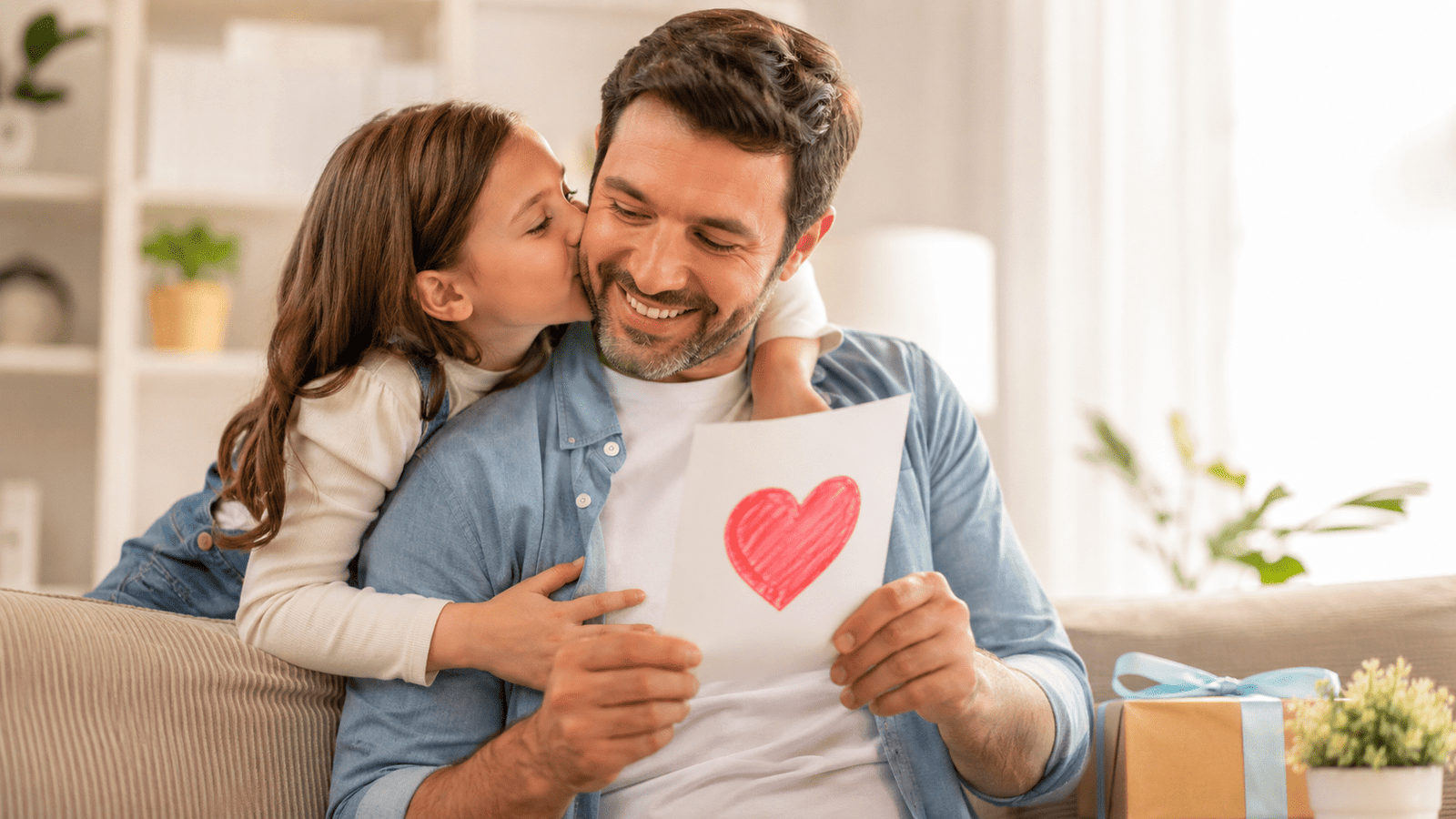 Papá sonríe mientras recibe una tarjeta del Día del Padre con un corazón dibujado y un beso de su hija