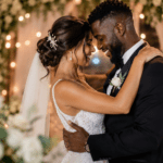 Pareja de novios abrazándose con alegría en una boda romántica con luces cálidas, flores blancas y ambiente elegante.