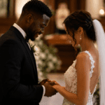 Pareja interracial de novios tomados de las manos durante una boda romántica, en un ambiente cálido con flores y velas.
