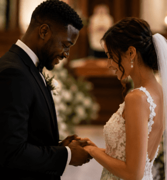 Pareja interracial de novios tomados de las manos durante una boda romántica, en un ambiente cálido con flores y velas.