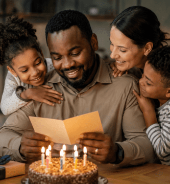 Papá afrodescendiente leyendo una tarjeta de cumpleaños junto a su familia y un pastel con velas