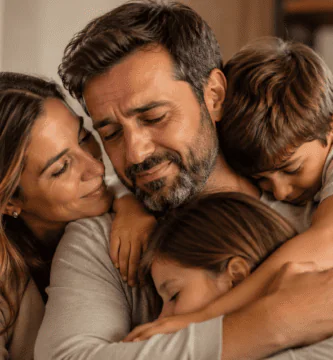 Esposo emocionado recibe el abrazo de su esposa e hijos en casa, imagen para poemas del Día del Padre que hagan llorar.