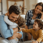 Esposo abrazando a sus hijos en casa mientras su pareja lo mira con amor, imagen cálida sobre un buen padre presente.