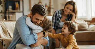 Esposo abrazando a sus hijos en casa mientras su pareja lo mira con amor, imagen cálida sobre un buen padre presente.