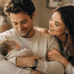 Esposo primerizo sosteniendo a su bebé junto a su esposa en un momento tierno del Día del Padre