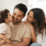Novio que es papá sonriendo con su hijo mientras su pareja lo acompaña con ternura en casa.