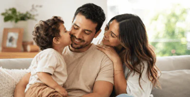 Novio que es papá sonriendo con su hijo mientras su pareja lo acompaña con ternura en casa.