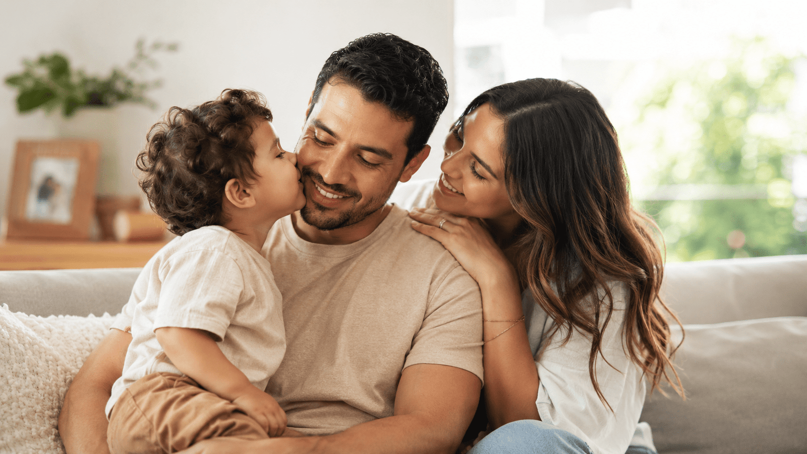Novio que es papá sonriendo con su hijo mientras su pareja lo acompaña con ternura en casa.
