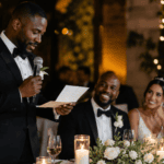 Padrino de boda leyendo un discurso emotivo para los novios durante una recepción elegante con luces cálidas y flores blancas.