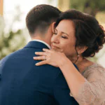 Madre abrazando emocionada a su hijo el día de su boda, en una escena cálida y familiar llena de orgullo y ternura.