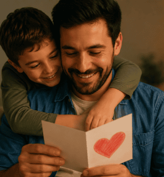 Niño abrazando a su papá mientras ambos observan una tarjeta con un corazón en una sala cálida.