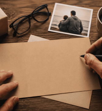 Manos escribiendo una tarjeta para papá junto a un regalo, una fotografía familiar y una taza de café