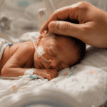 Bebé prematuro descansando en incubadora mientras una mano adulta lo acaricia con ternura
