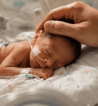 Bebé prematuro descansando en incubadora mientras una mano adulta lo acaricia con ternura