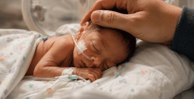 Bebé prematuro descansando en incubadora mientras una mano adulta lo acaricia con ternura