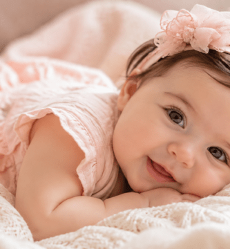 Bebé niña sonriente recostada sobre una manta clara en un ambiente cálido y delicado