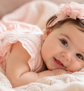Bebé niña sonriente recostada sobre una manta clara en un ambiente cálido y delicado