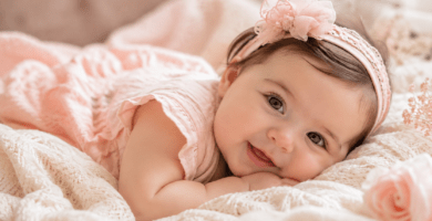 Bebé niña sonriente recostada sobre una manta clara en un ambiente cálido y delicado