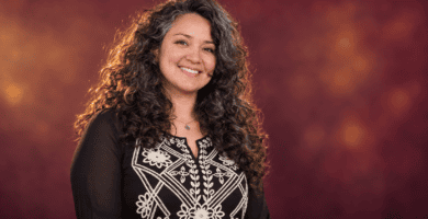 Diana Paola Agámez con cabello rizado y blusa negra bordada sobre un fondo burdeos.